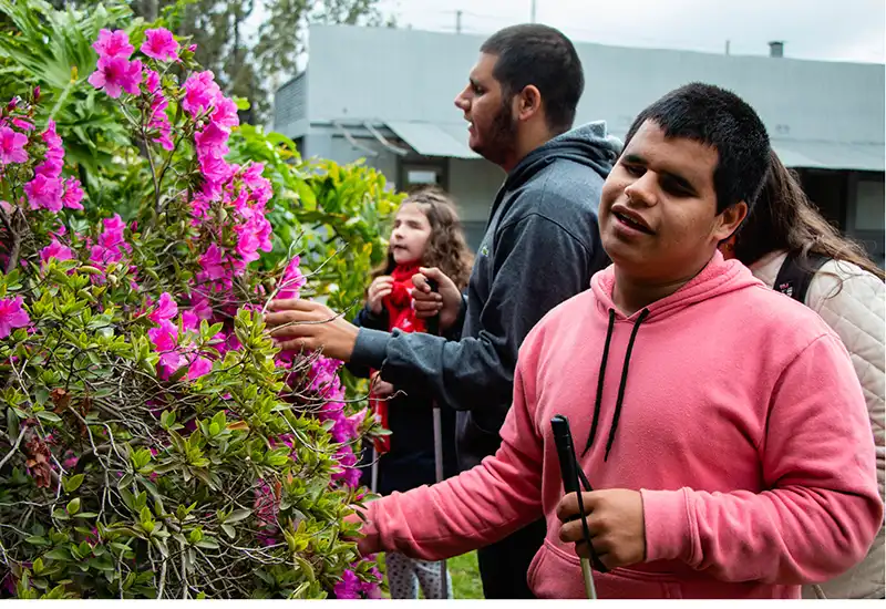 un joven ciego disfruta tocando y reconociendo las flores del parque