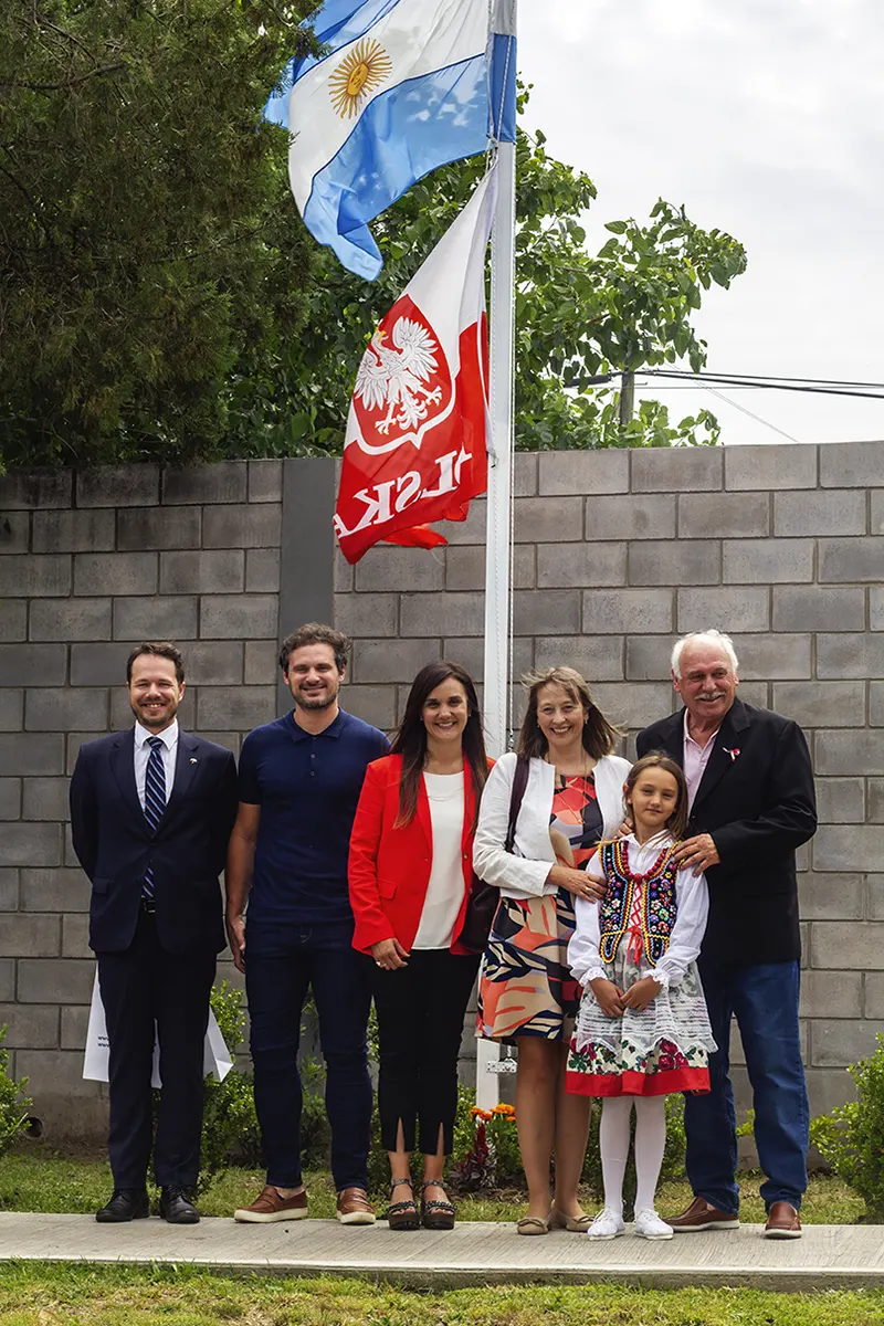 Miguel y Micaela Szykula junto a la embajadora bajo el mástil con las banderas de Argentina y Polonia.