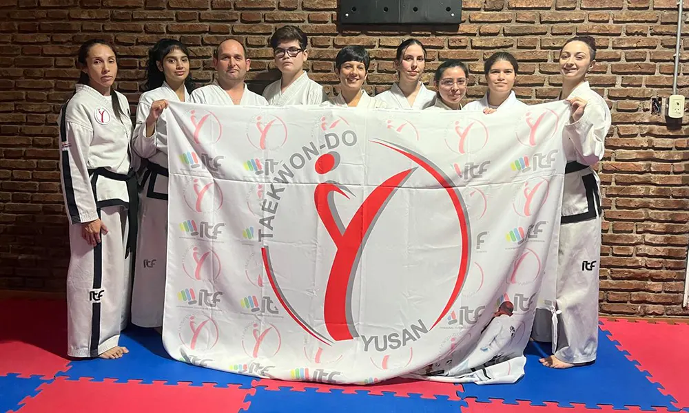 Deportistas de la asociación de taekwondo YUSAN posando junto a su bandera