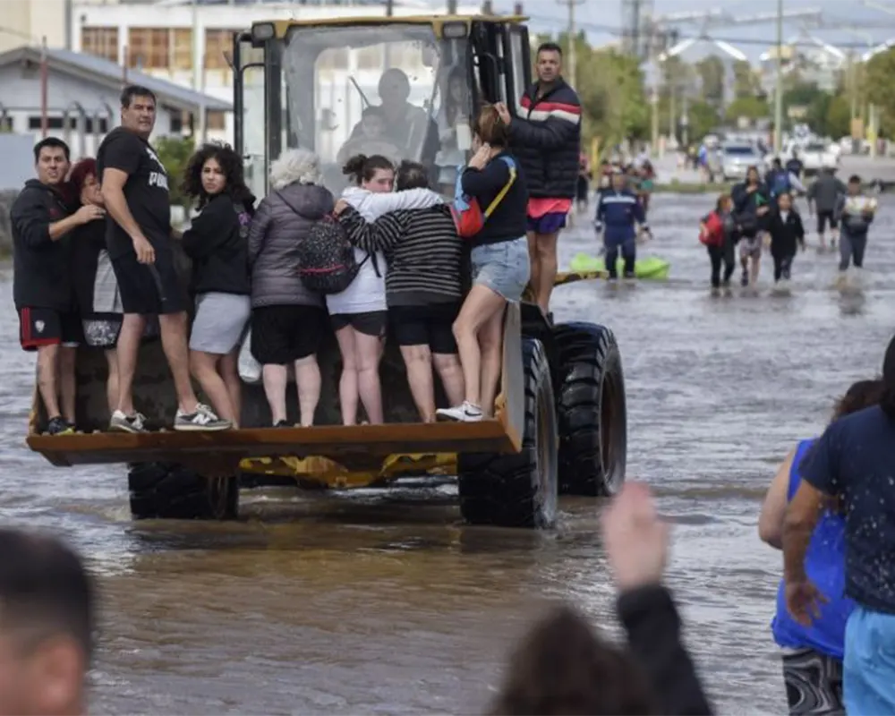 Gente subida a una pala mecanica, saliendo de zonas inundadas en bahía blanca