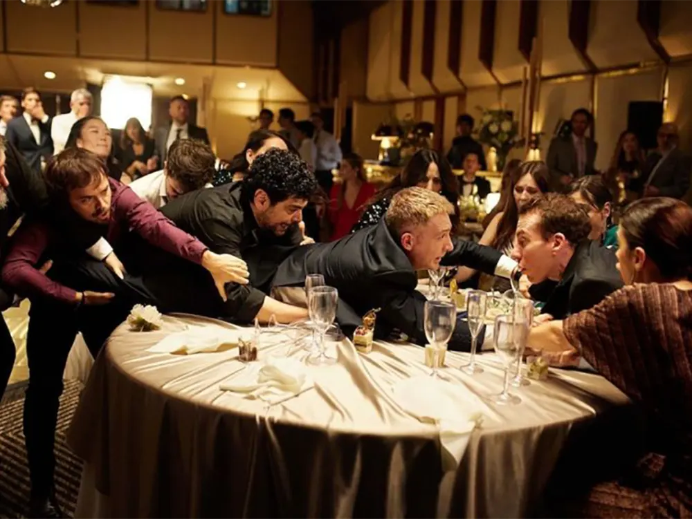 Escena familiar dramática, los protagonistas discuten acaloradamente durante una boda,  sobre una mesa.