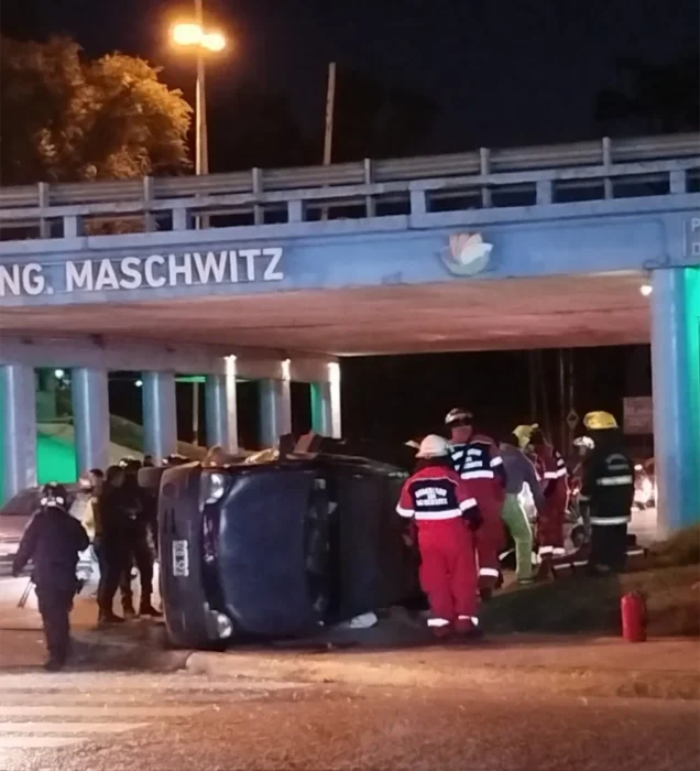 Personal de bomberos y policías alrededor del auto que volcó bajo el puente