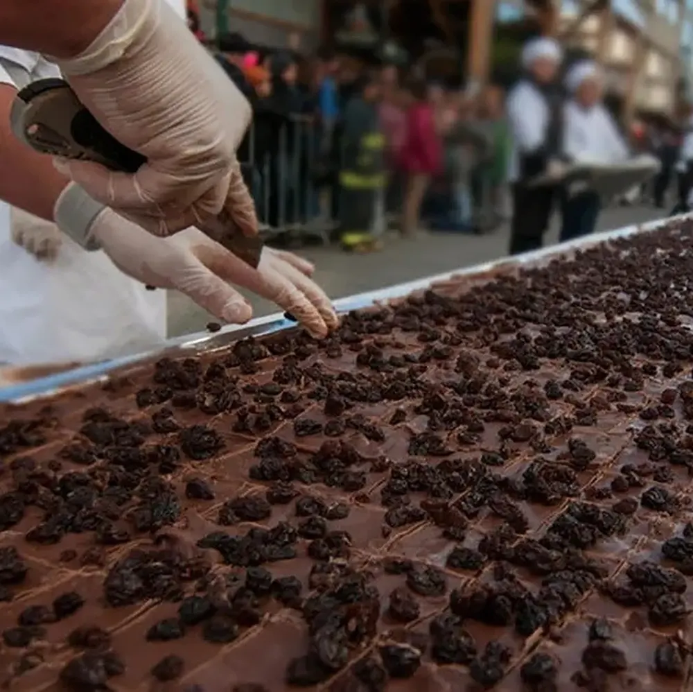 pastelero cortando una gran bandejas de chocolate artesanal con un cutter