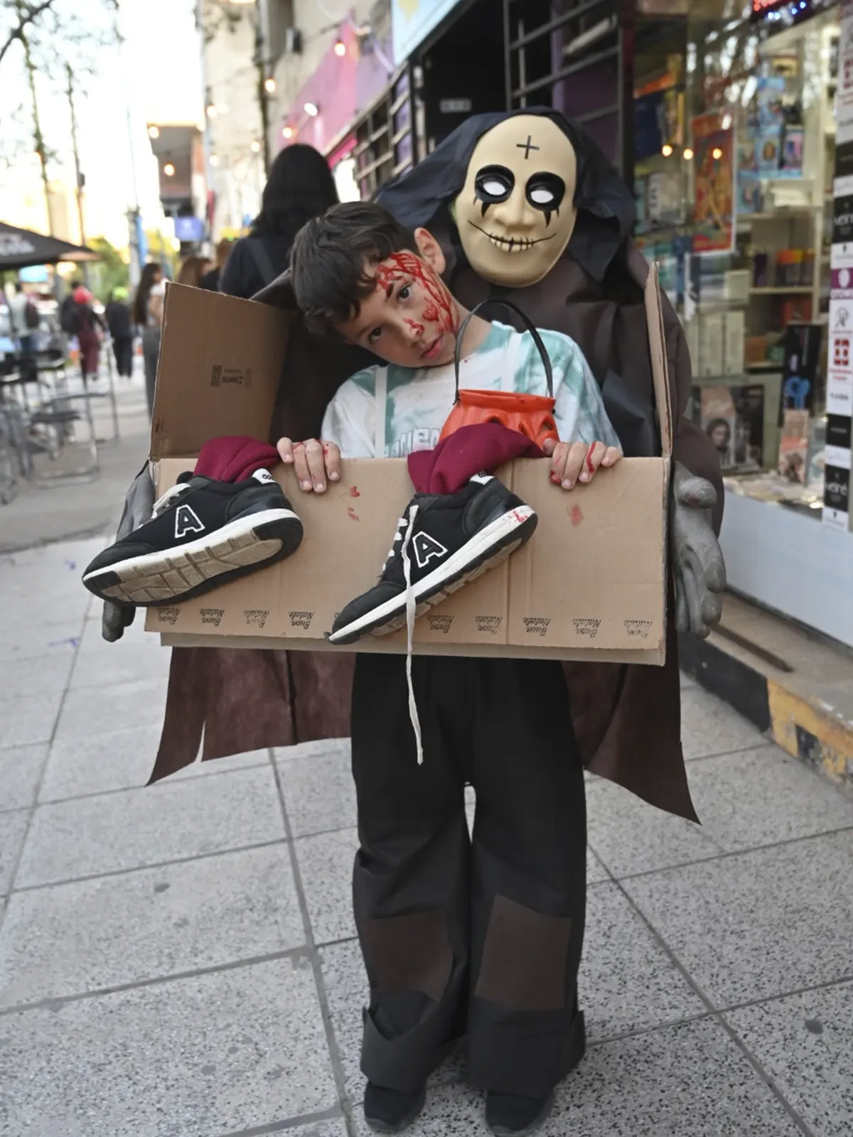 Niño disfrazado se sostiene de una caja como si le levara la muerte.