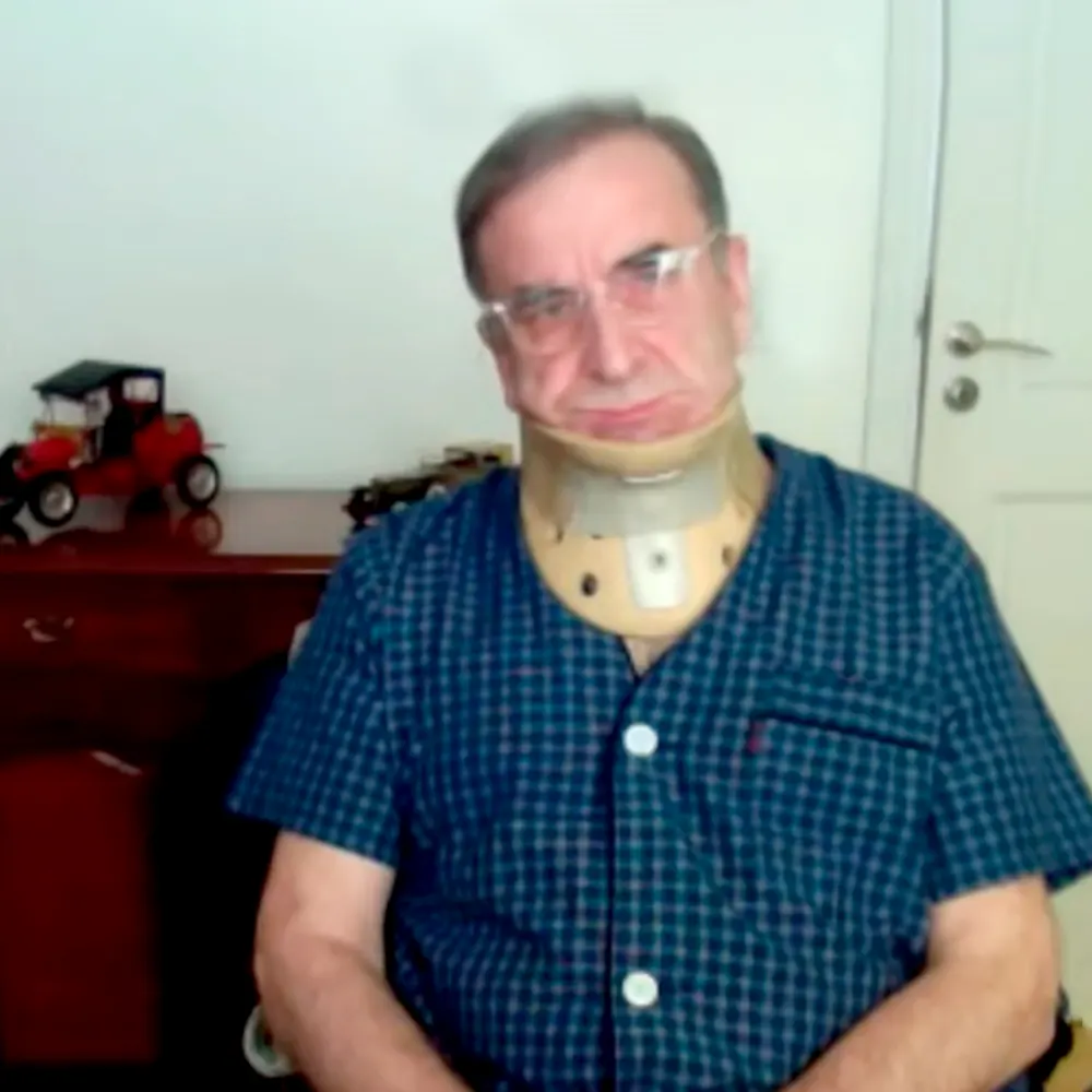 Luis Patti en silla de ruedas y con cuello ortopédico, en una audiencia judicial virtual