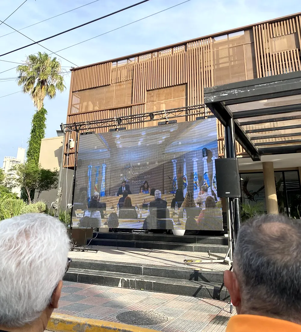 Militantes y familiares de los concejales electos miran la sesión en una pantalla gigante colocada en la calle